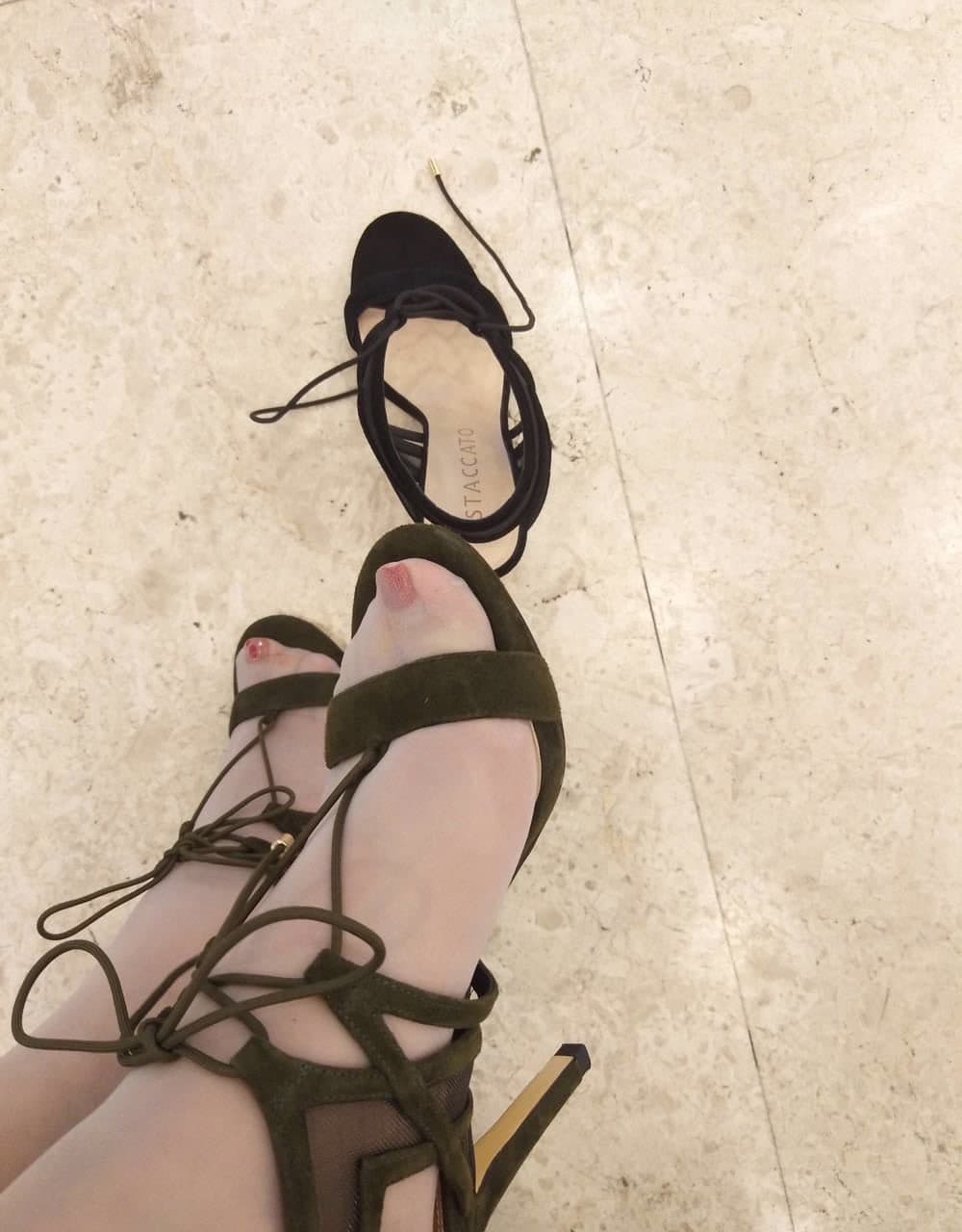 Side detail of nude foot arched inside a strappy open-toe heel on a marble floor